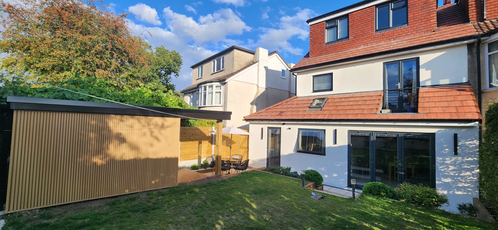White rendered rear extension with dark framed glazing, tiled roof and landscaped garden.